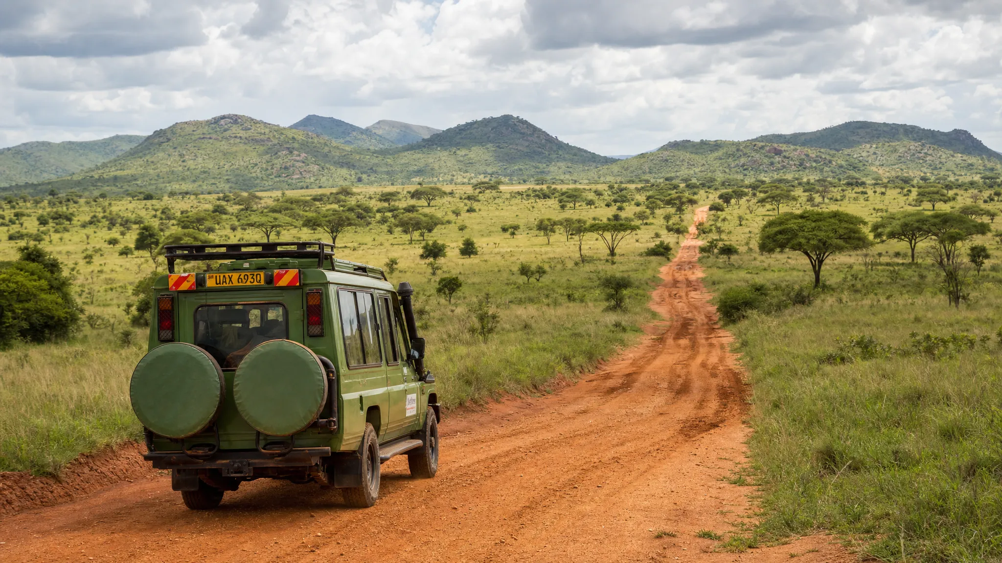 A 4x4 safari vehicle on a red dirt road in Uganda, with open savanna, acacia trees, and distant green hills, showing the road and landscape conditions travelers compare when choosing between guided safari tours and self-drive.